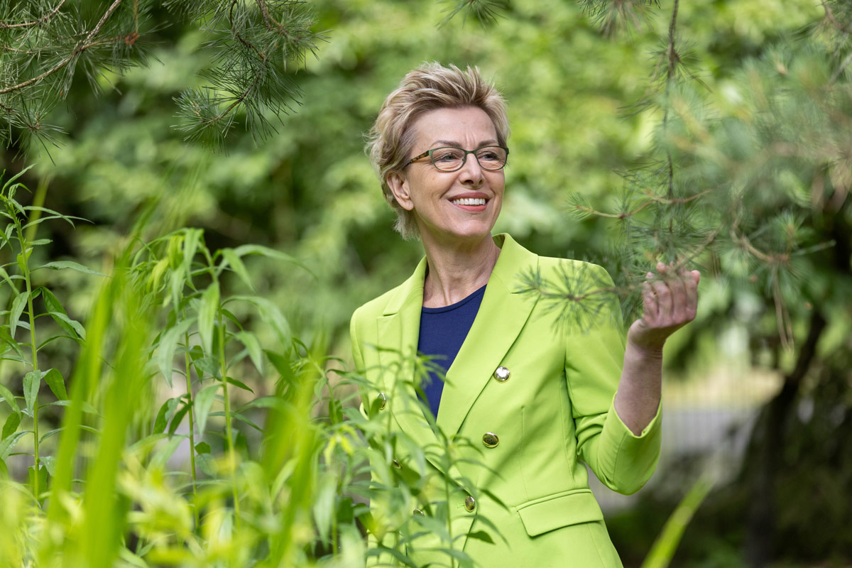 Ein junger dunkelhaariger Mann steht hinter einem Tresen, vor ihm liegt ein Stadtplan. Er lächelt und deutet mit einem Stift auf die Mitte des Planes und erteilt damit einer Frau Auskunft, die sich rechts im Vordergrund des Bildes befindet und ebenfalls auf den Plan blickt.